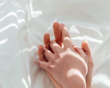 partial view of loving couple holding hands while lying on white bed sheet